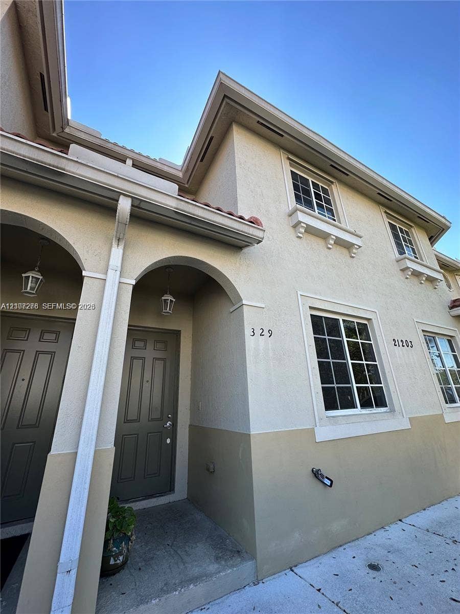 Stucco exterior featuring arched entryways, multi-pane windows with decorative molding, and wall-mounted outdoor lighting fixtures