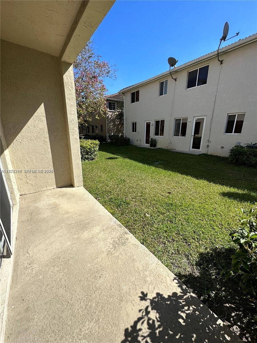Concrete patio slab extending toward a lawn area with perimeter shrubbery and stucco exterior finish