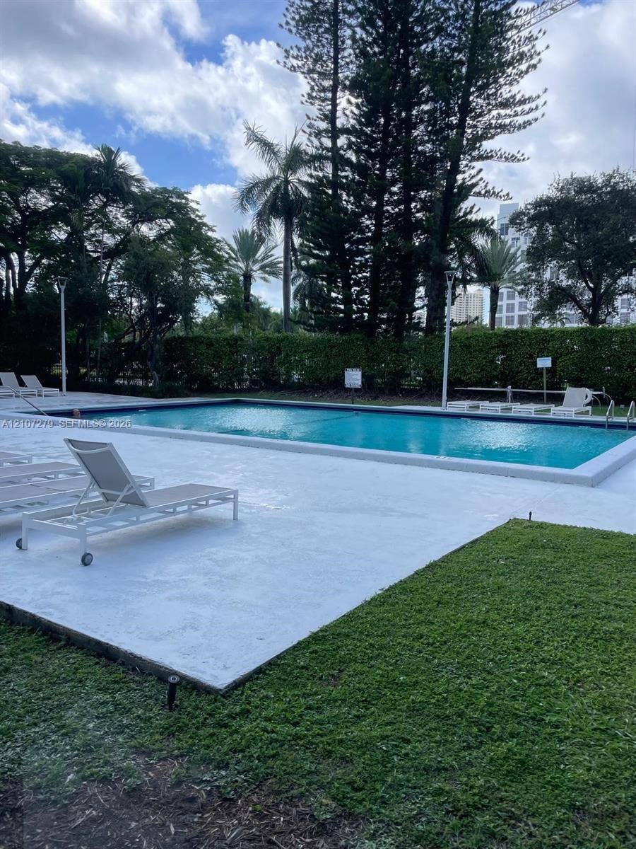 20100 W Country Club Drive, #601, Aventura, FL 33180 Rectangular swimming pool surrounded by a concrete deck, manicured lawn, perimeter landscaping, and mature trees
