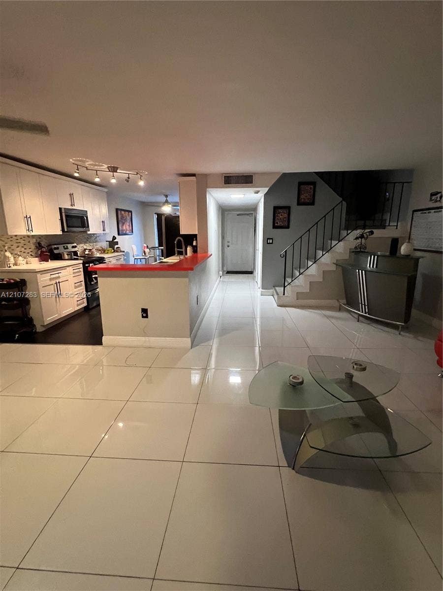 3301 Raleigh Street, #4E, Hollywood, FL 33021 Kitchen featuring white cabinetry, solid-surface countertops, and built-in stainless steel appliances, complemented by large-format tile flooring and an open staircase with wrought-iron railing