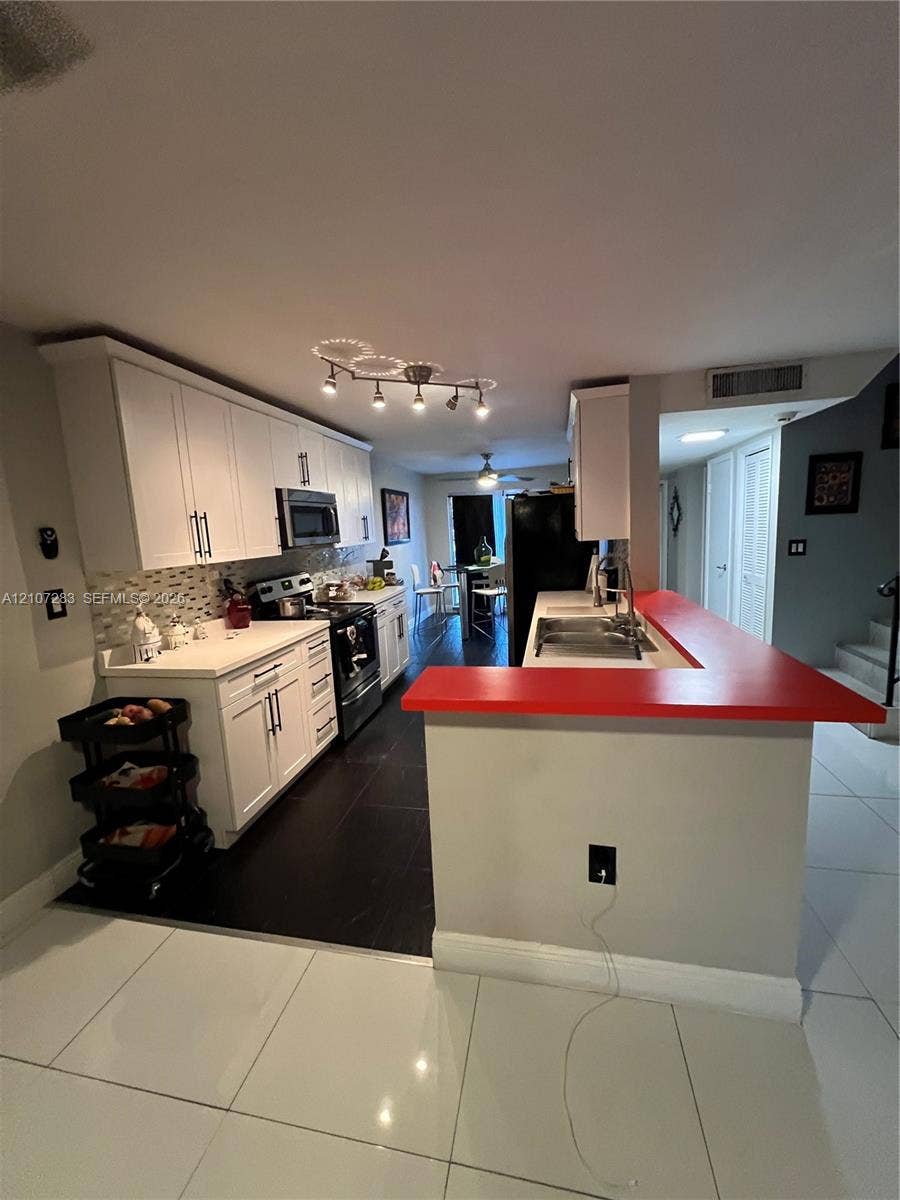 3301 Raleigh Street, #4E, Hollywood, FL 33021 Kitchen featuring white shaker-style cabinetry, a contrasting red peninsula countertop, dark tile flooring, a multi-bulb track lighting fixture, and a tile backsplash