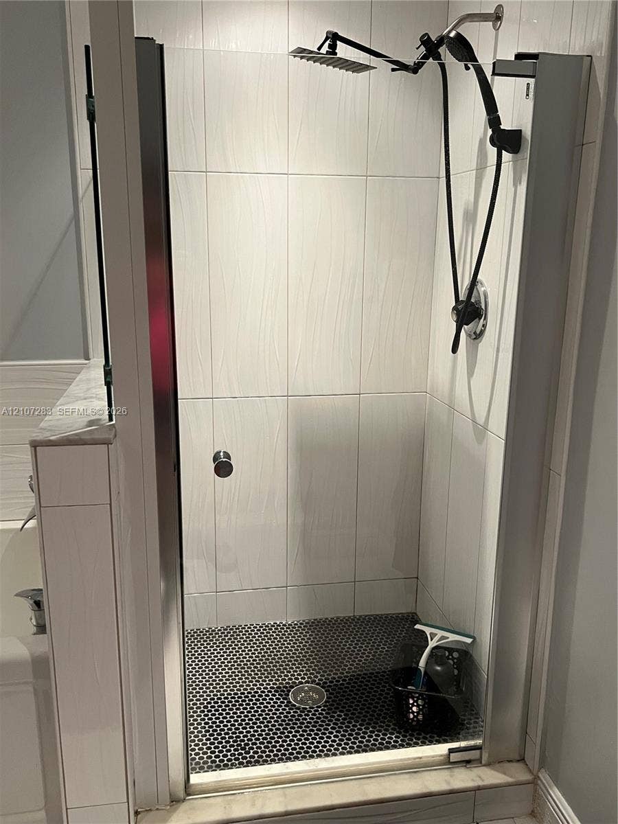 3301 Raleigh Street, #4E, Hollywood, FL 33021 Walk-in shower featuring a frameless glass door, textured white wall tile, dark penny-round floor tile, and a dual-head rainfall shower fixture