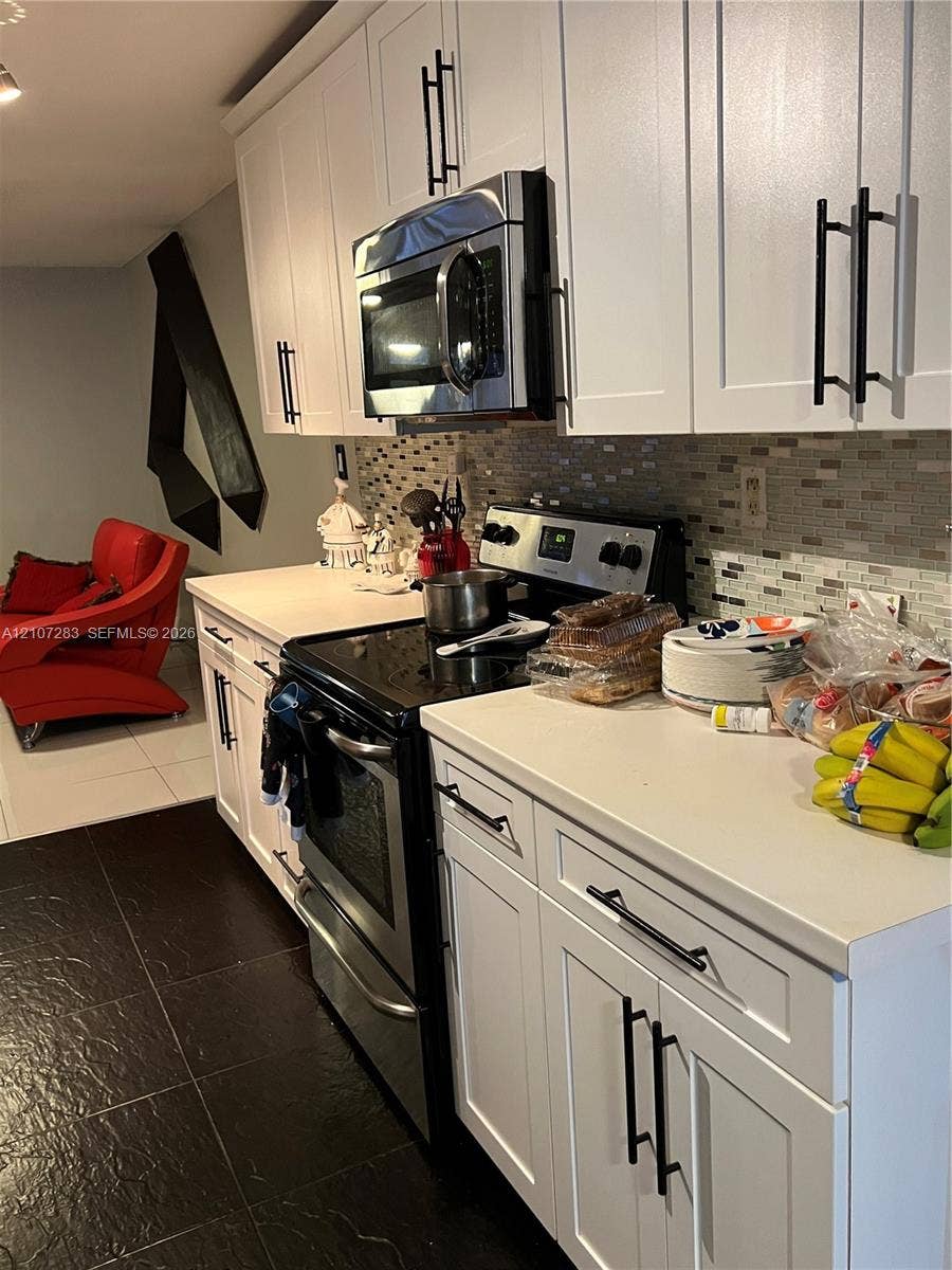 3301 Raleigh Street, #4E, Hollywood, FL 33021 White shaker-style cabinetry with matte black pulls, solid surface countertops, a mosaic tile backsplash, and stainless steel kitchen appliances