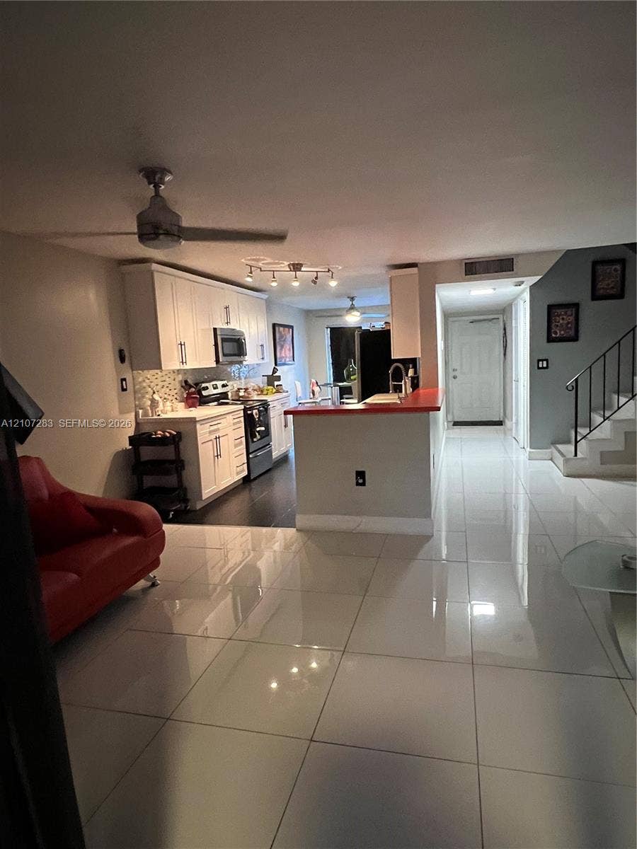 3301 Raleigh Street, #4E, Hollywood, FL 33021 Large-format tile flooring, white cabinetry, integrated kitchen peninsula, ceiling fans, and staircase with iron railing
