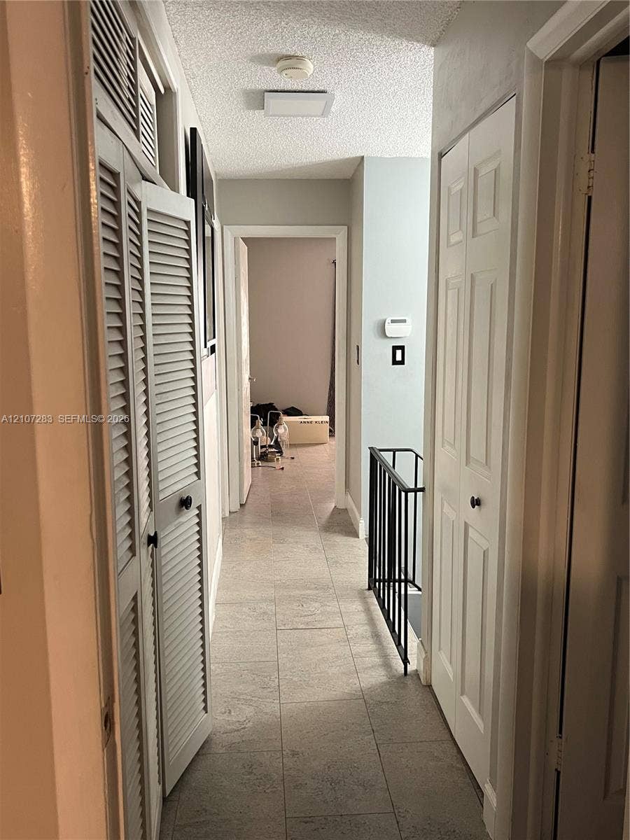 3301 Raleigh Street, #4E, Hollywood, FL 33021 Hallway featuring large-format tile flooring, white bi-fold closet doors, louvered closet cabinetry, and a black metal railing