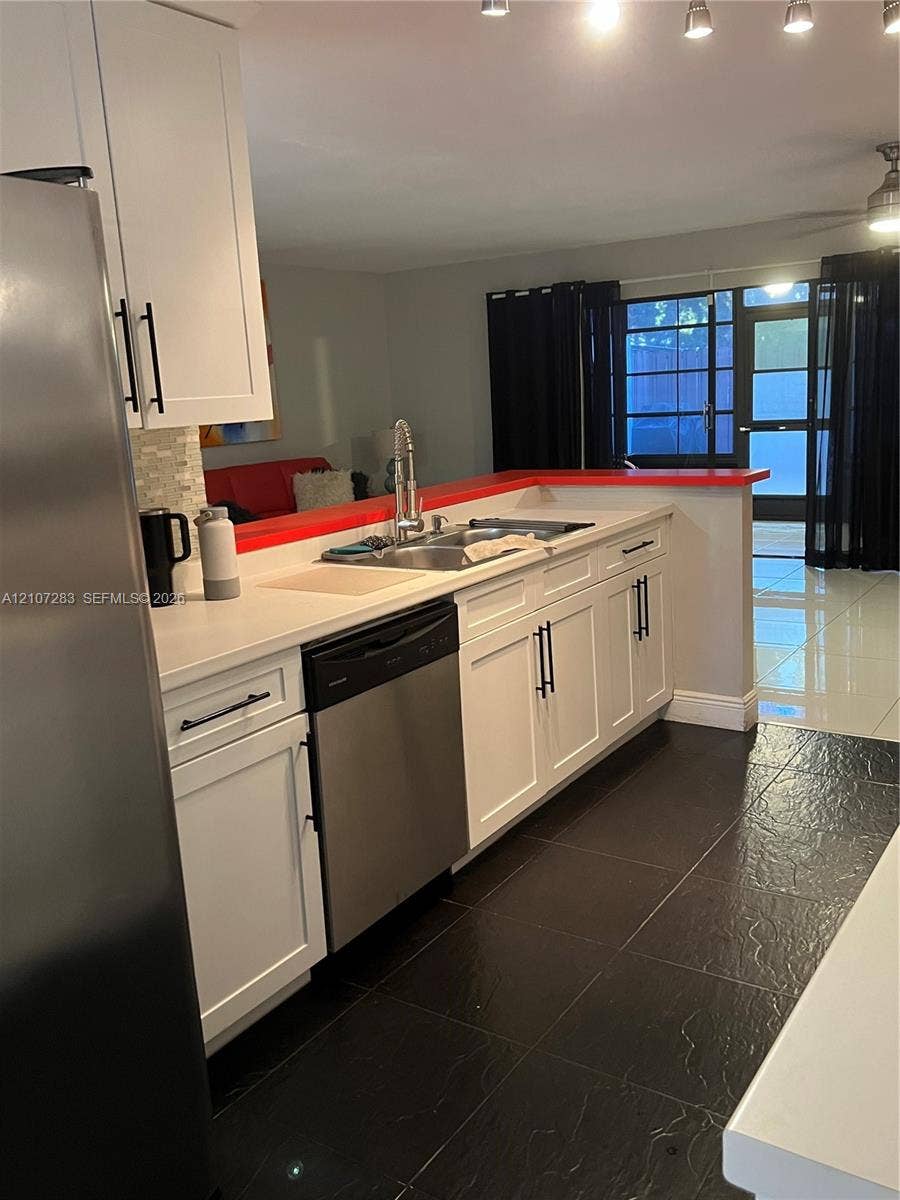 3301 Raleigh Street, #4E, Hollywood, FL 33021 Kitchen featuring white shaker-style cabinetry, stainless steel appliances, a dual-basin sink with a gooseneck faucet, a mosaic tile backsplash, and dark tile flooring