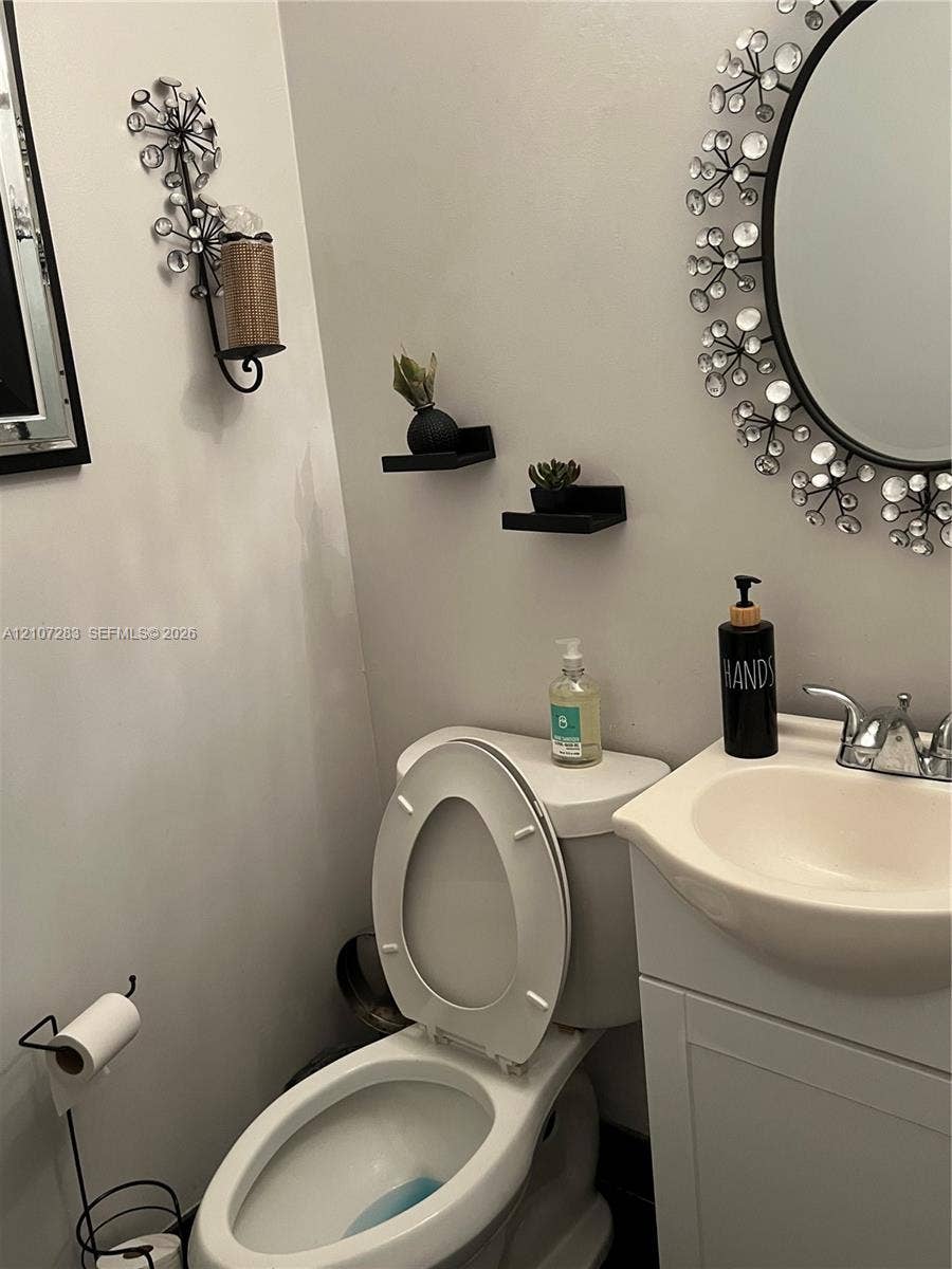 3301 Raleigh Street, #4E, Hollywood, FL 33021 Vanity featuring a molded-top sink with metallic-finish faucet, accompanied by two wall-mounted floating shelves and a circular wall mirror with decorative surround