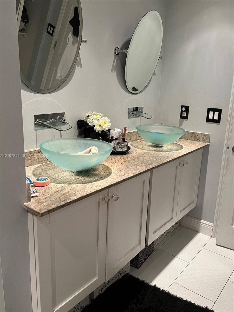 3301 Raleigh Street, #4E, Hollywood, FL 33021 Dual vanity featuring white shaker-style cabinetry, a stone countertop, wall-mounted faucets, frosted glass vessel sinks, and oval mirrors
