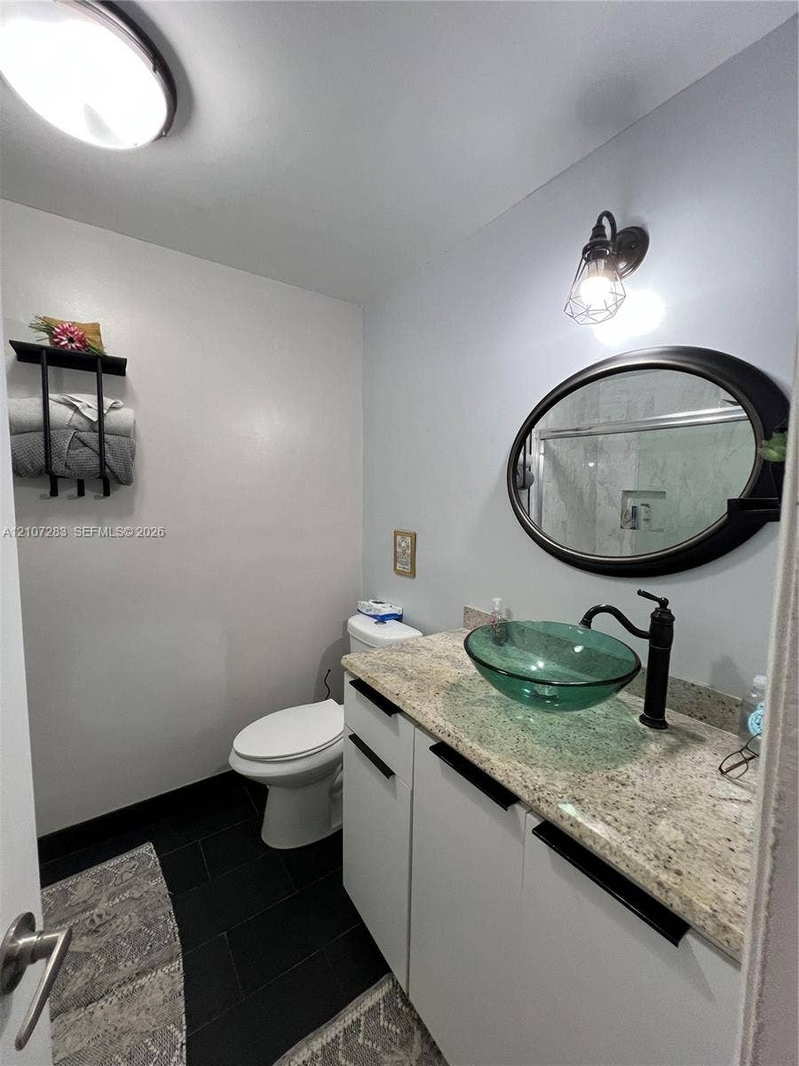 3301 Raleigh Street, #4E, Hollywood, FL 33021 Stone countertop with a glass vessel sink, matte black faucet, oval wall mirror, and dark tile flooring
