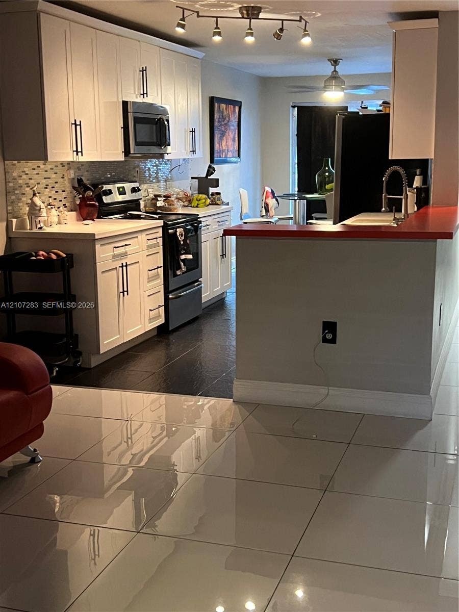 3301 Raleigh Street, #4E, Hollywood, FL 33021 Kitchen featuring white cabinetry with matte black hardware, tiled backsplash, solid surface countertops, and dark floor tiling