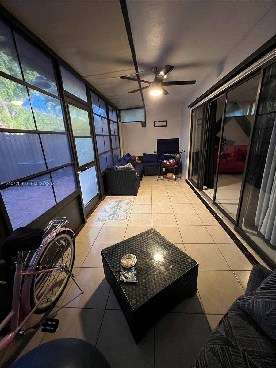 3301 Raleigh Street, #4E, Hollywood, FL 33021 Enclosed patio featuring grid-patterned window panels, large-format tile flooring, sliding glass door entry, and a ceiling-mounted light fixture with a fan