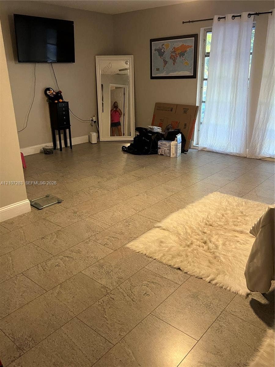 3301 Raleigh Street, #4E, Hollywood, FL 33021 Living area featuring neutral-toned tile flooring and glass paneled doors with a curtain rod fixture