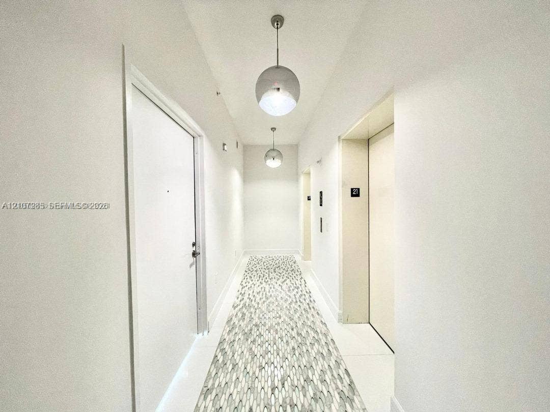 2020 N Bayshore Drive, #2102, Miami, FL 33137 Hallway featuring crisp white walls, large-format tile flooring with a patterned mosaic inlay, and dual spherical pendant lighting fixtures