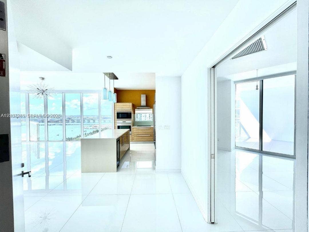 2020 N Bayshore Drive, #2102, Miami, FL 33137 Open-concept kitchen featuring light wood-finish cabinetry, a central island with a stone countertop, built-in stainless steel appliances, white tile flooring, and floor-to-ceiling windows