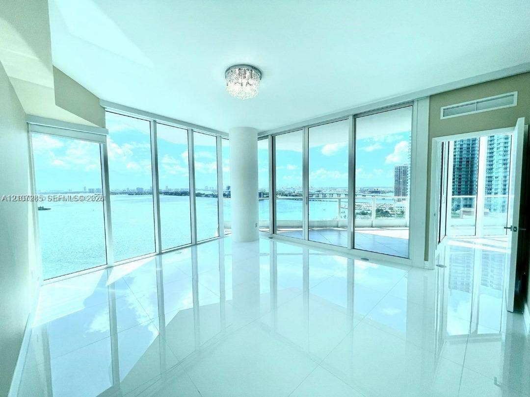 2020 N Bayshore Drive, #2102, Miami, FL 33137 Floor-to-ceiling glass walls, polished white tile flooring, wraparound balcony, and crystal flush-mount ceiling fixture