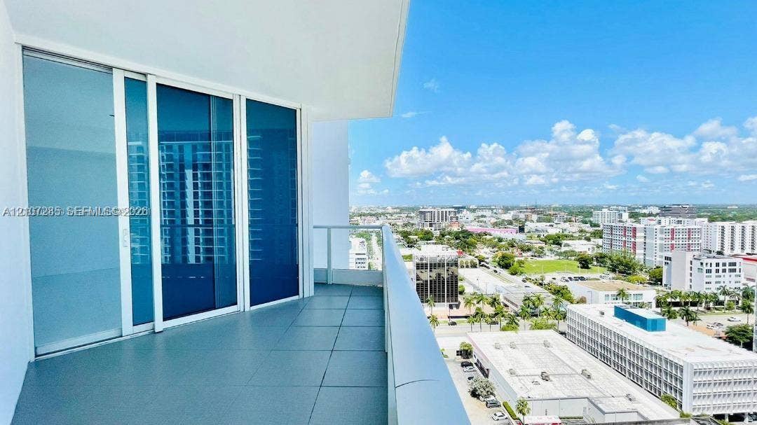 2020 N Bayshore Drive, #2102, Miami, FL 33137 Covered balcony featuring large-format tile flooring and a glass-paneled railing, accessible through expansive floor-to-ceiling sliding glass doors