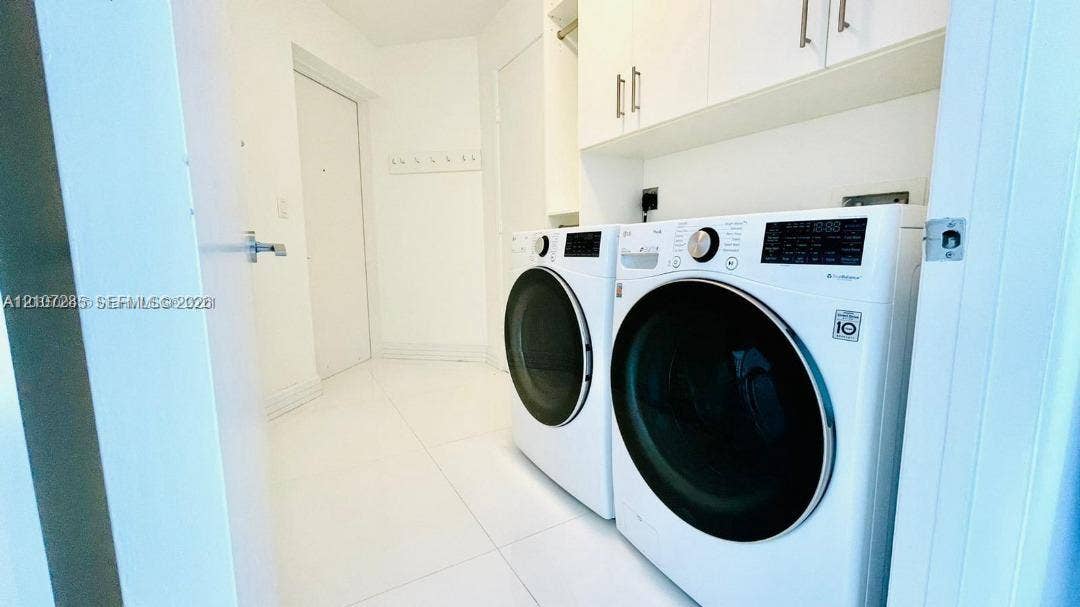 2020 N Bayshore Drive, #2102, Miami, FL 33137 Laundry area featuring white large-format tile flooring, built-in upper cabinetry with brushed metal hardware, and a side-by-side front-loading washer and dryer set