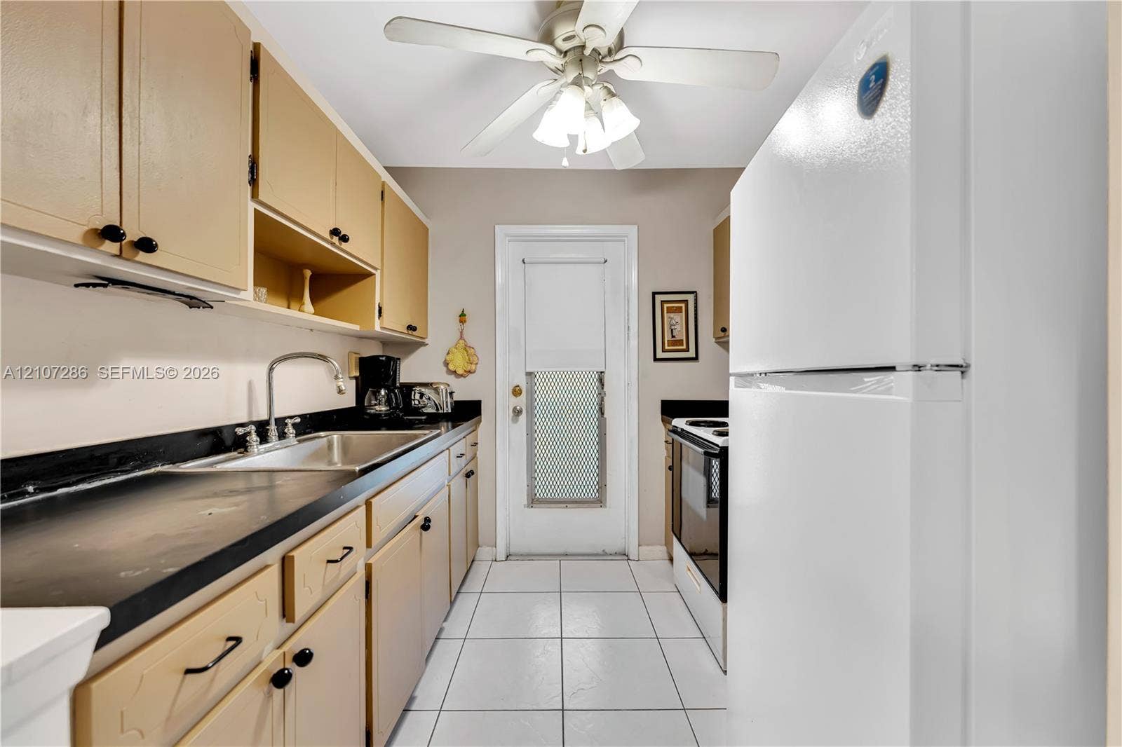 2458 Polk Street, #206, Hollywood, FL 33020 Kitchen featuring cabinetry with contrasting dark countertops, integrated stainless steel sink with goose-neck faucet, white tile flooring, and a ceiling-mounted light fixture with fan