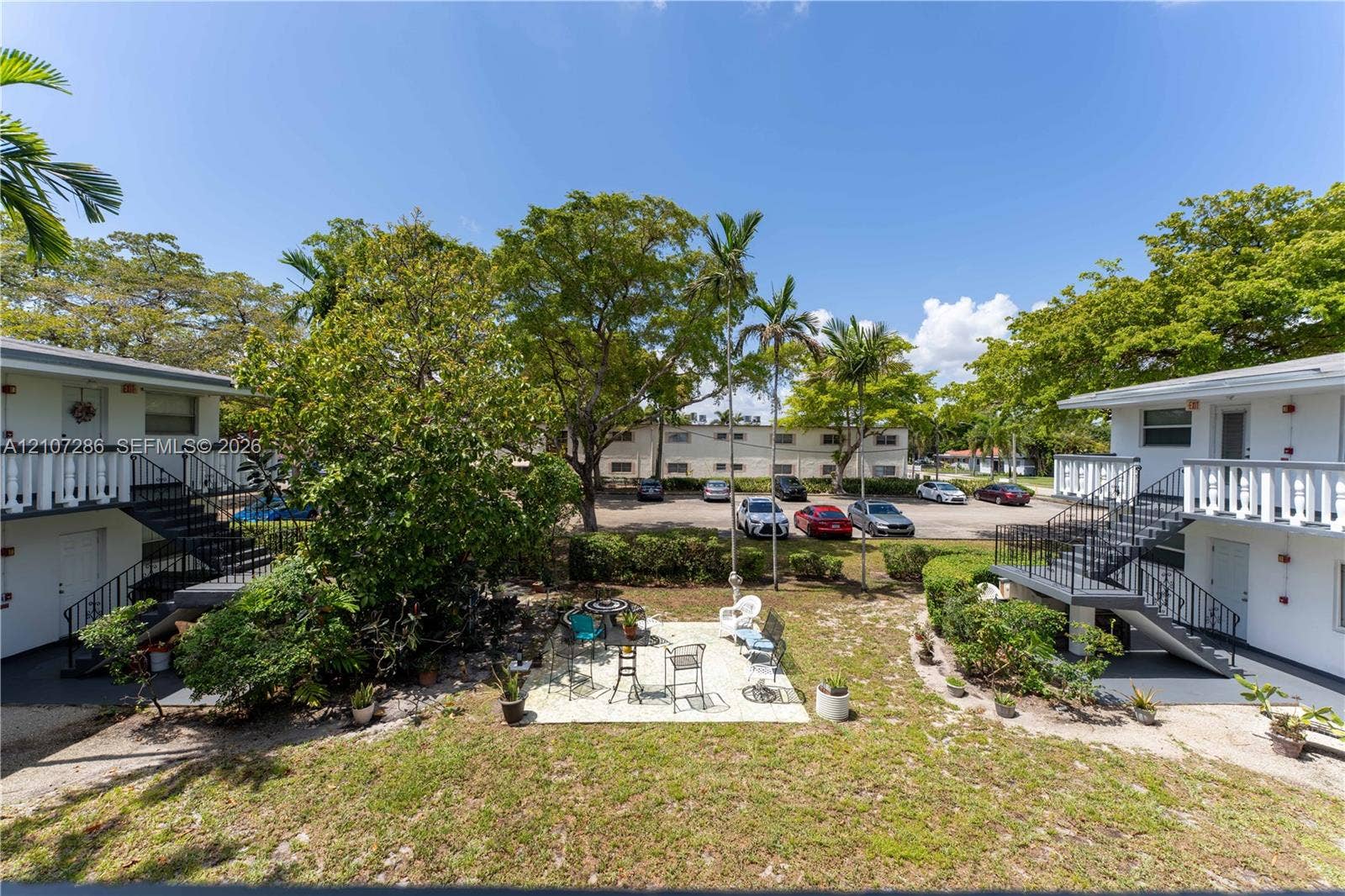 2458 Polk Street, #206, Hollywood, FL 33020 Exterior grounds featuring a paved patio, mature trees, manicured landscaping, metal exterior staircases, and white balustrade railings
