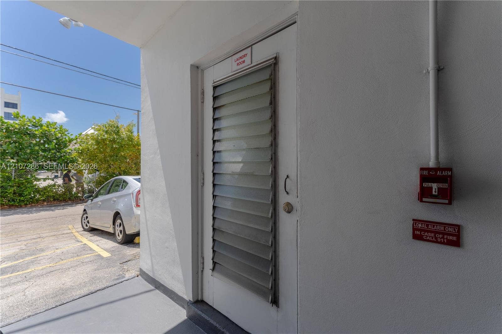 2458 Polk Street, #206, Hollywood, FL 33020 Exterior door featuring integrated jalousie window panels, smooth stucco wall finish, and a mounted fire alarm system