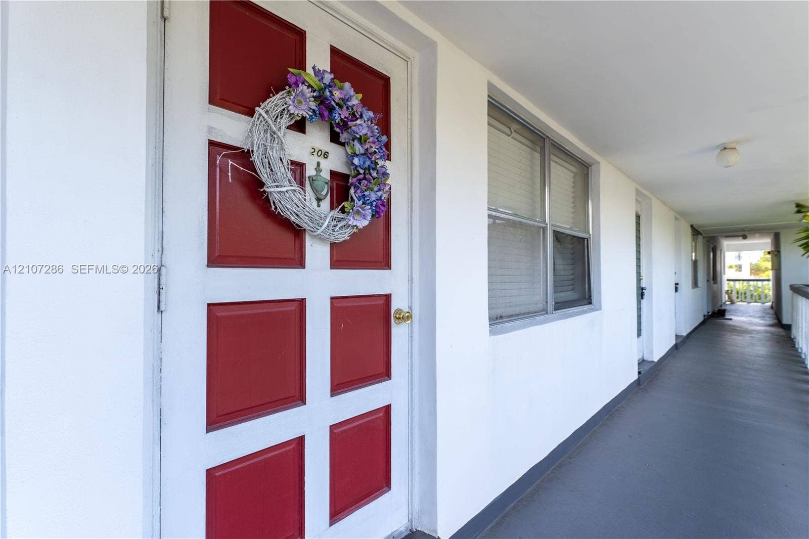 2458 Polk Street, #206, Hollywood, FL 33020 Red-painted six-panel entry door with metallic door knocker and brass-finish hardware, white stucco exterior wall, and window with white frame