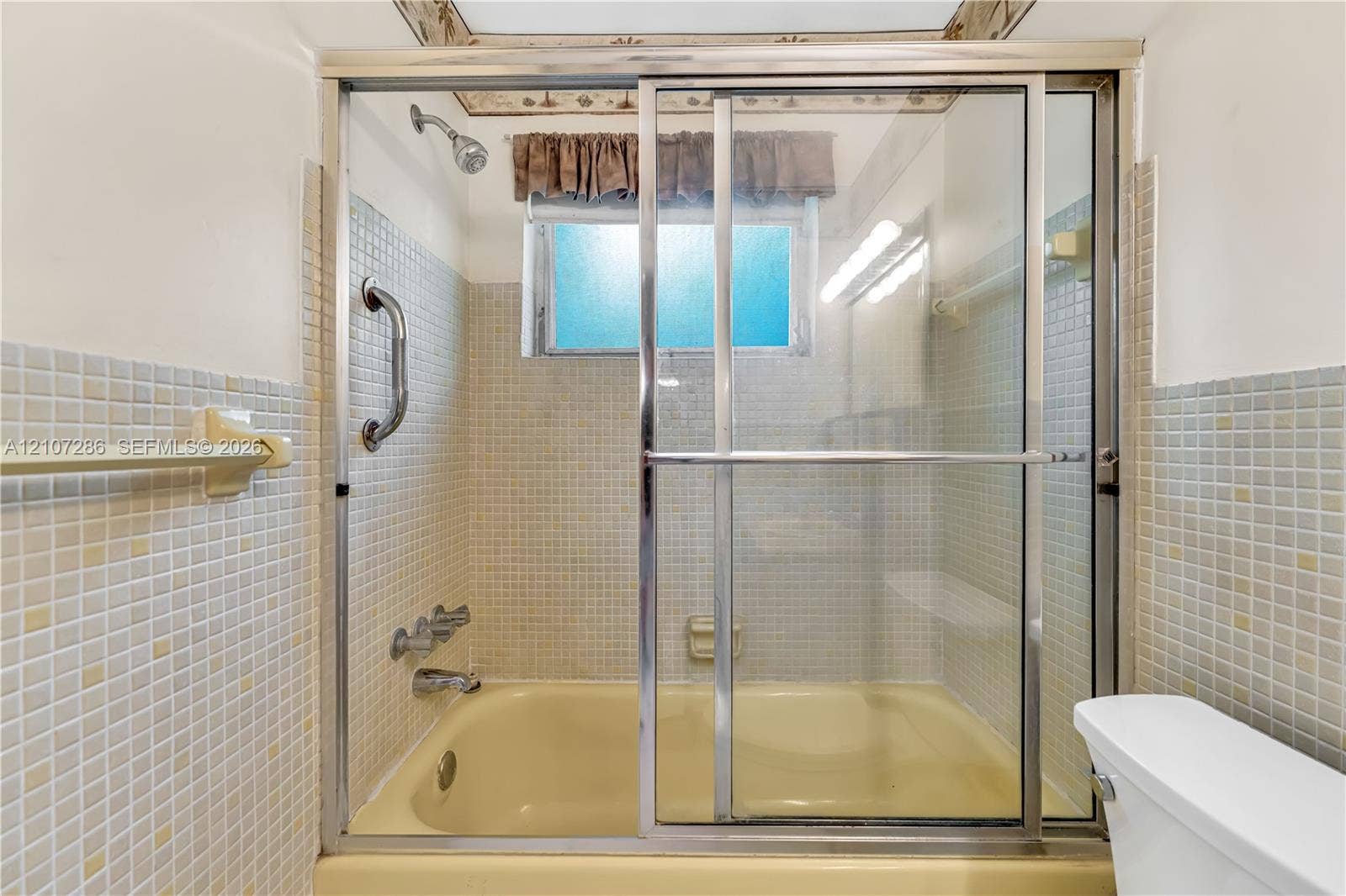 2458 Polk Street, #206, Hollywood, FL 33020 Bathtub featuring a glass sliding enclosure, mounted chrome faucet fixtures, and square mosaic wall tile surrounds