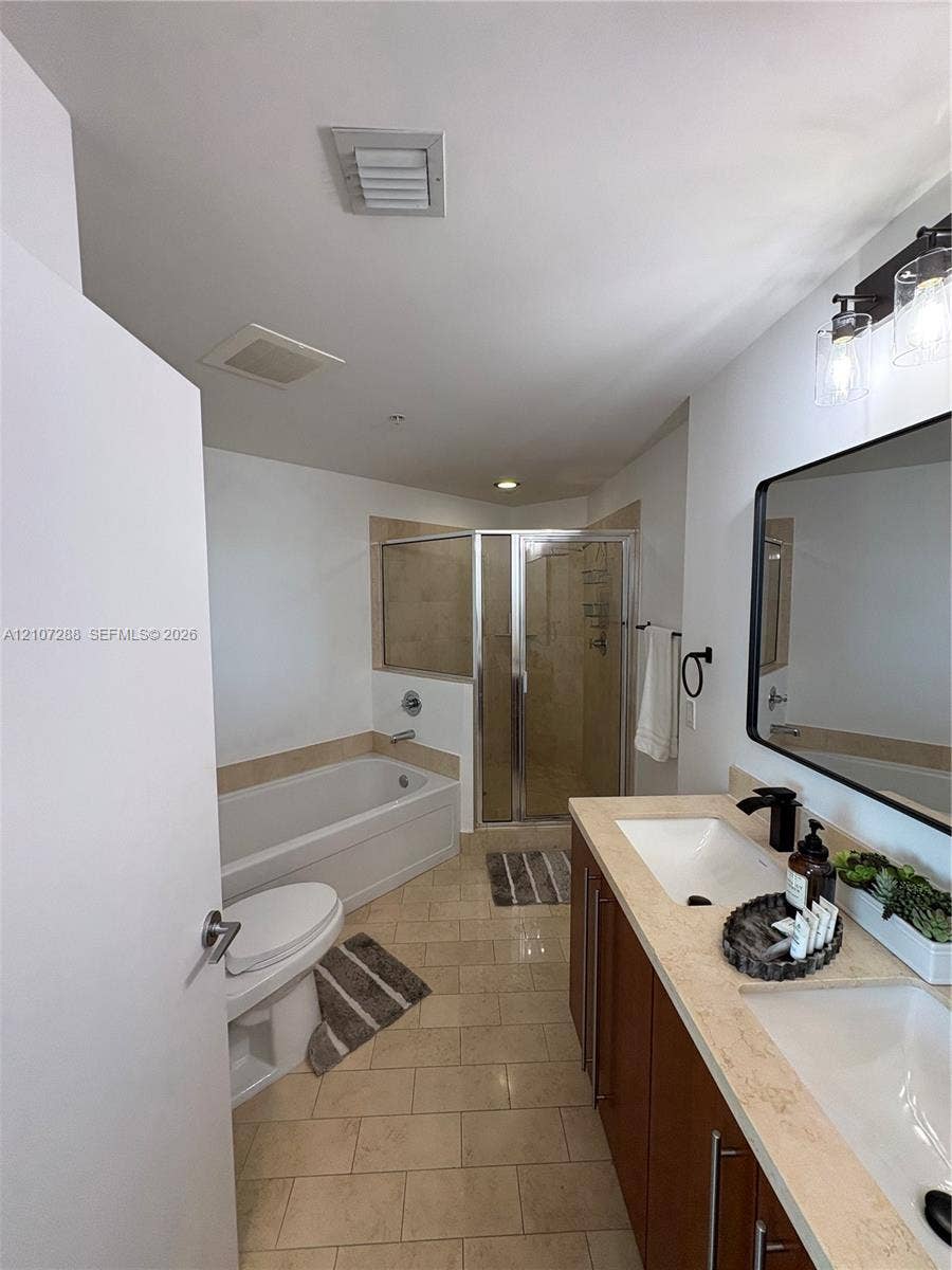 Double vanity with stone-surfaced countertop, dual under-mount sinks, rectangular mirror with black frame, separate glass-enclosed shower, and built-in soaking tub