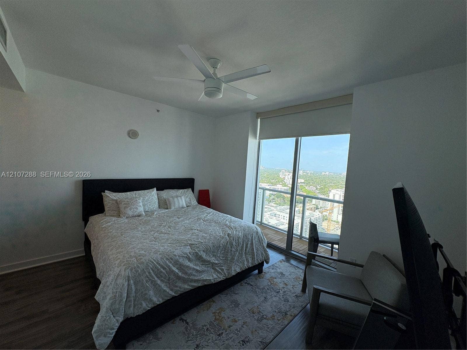 Floor-to-ceiling glass sliding door, expansive balcony, wood-finish flooring, and white ceiling fan
