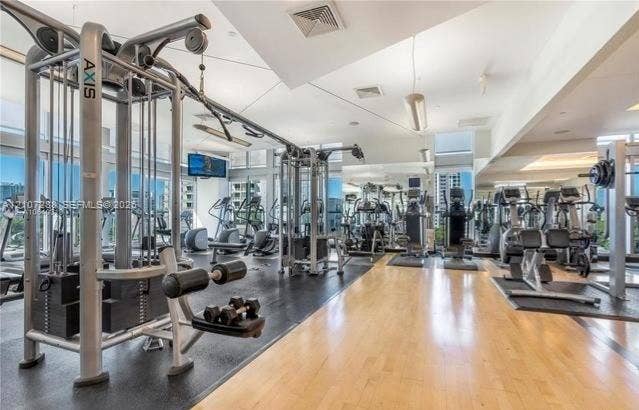Fitness facility featuring floor-to-ceiling windows, mirrored wall panels, multi-station exercise equipment, and a combination of wood-finish and rubberized flooring