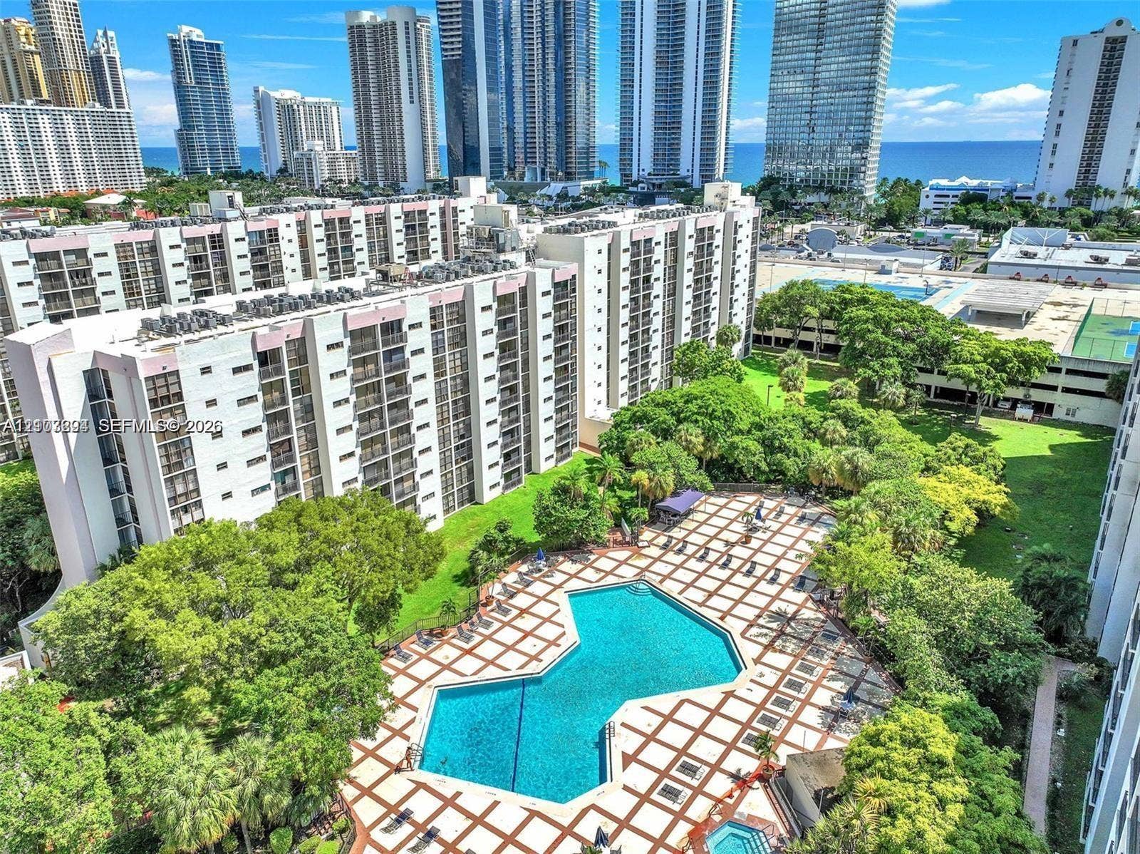 17021 N Bay Road, #219, Sunny Isles Beach, Sunny Isles Beach, FL 33160 Expansive swimming pool with geometric tile surround, lush landscaped grounds, mature trees, and high-rise skyline backdrop