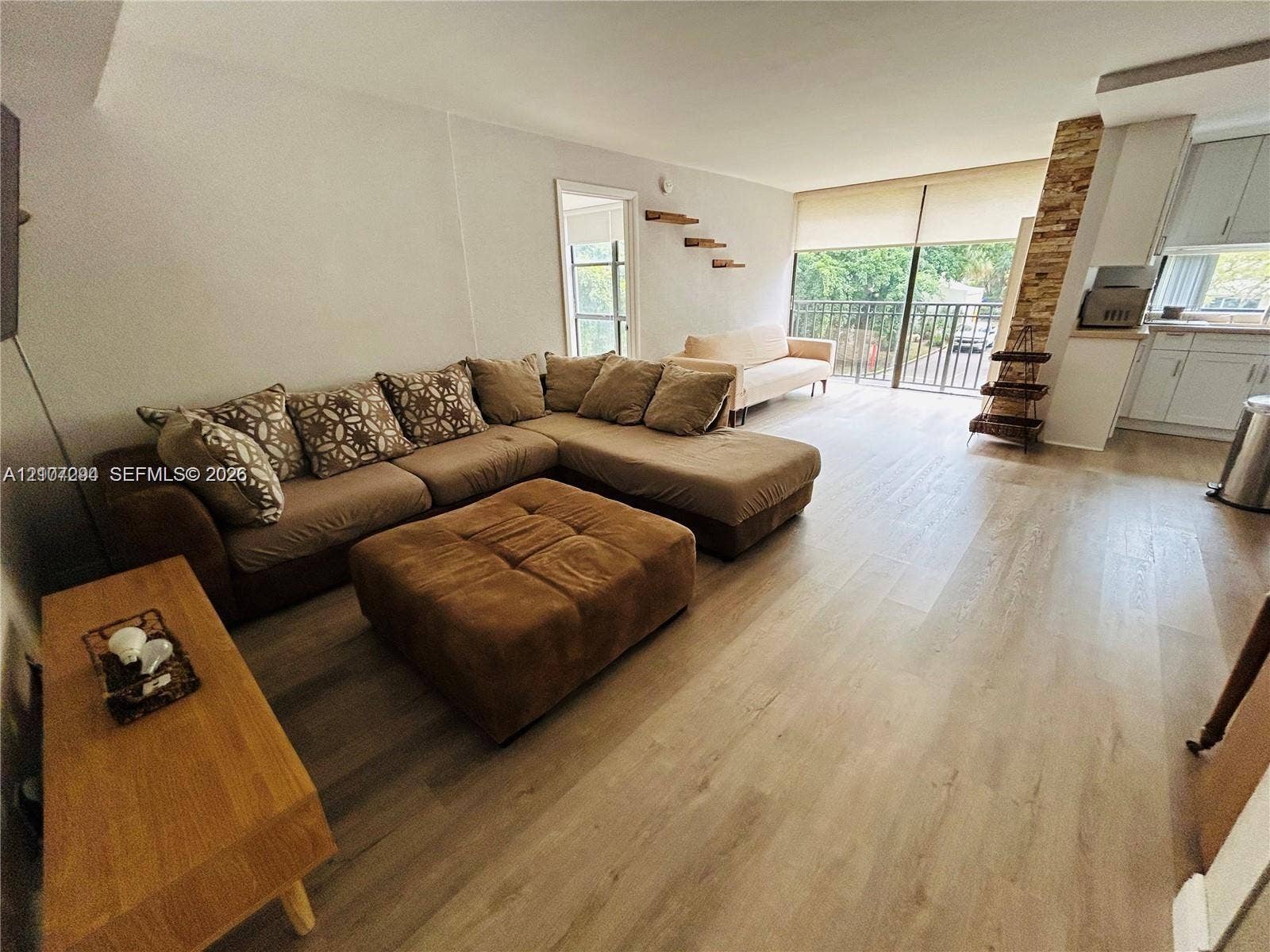 17021 N Bay Road, #219, Sunny Isles Beach, Sunny Isles Beach, FL 33160 Open-concept interior featuring wood-finish flooring, a floor-to-ceiling stone accent column, sliding glass doors to a balcony, and white cabinetry with a quartz countertop