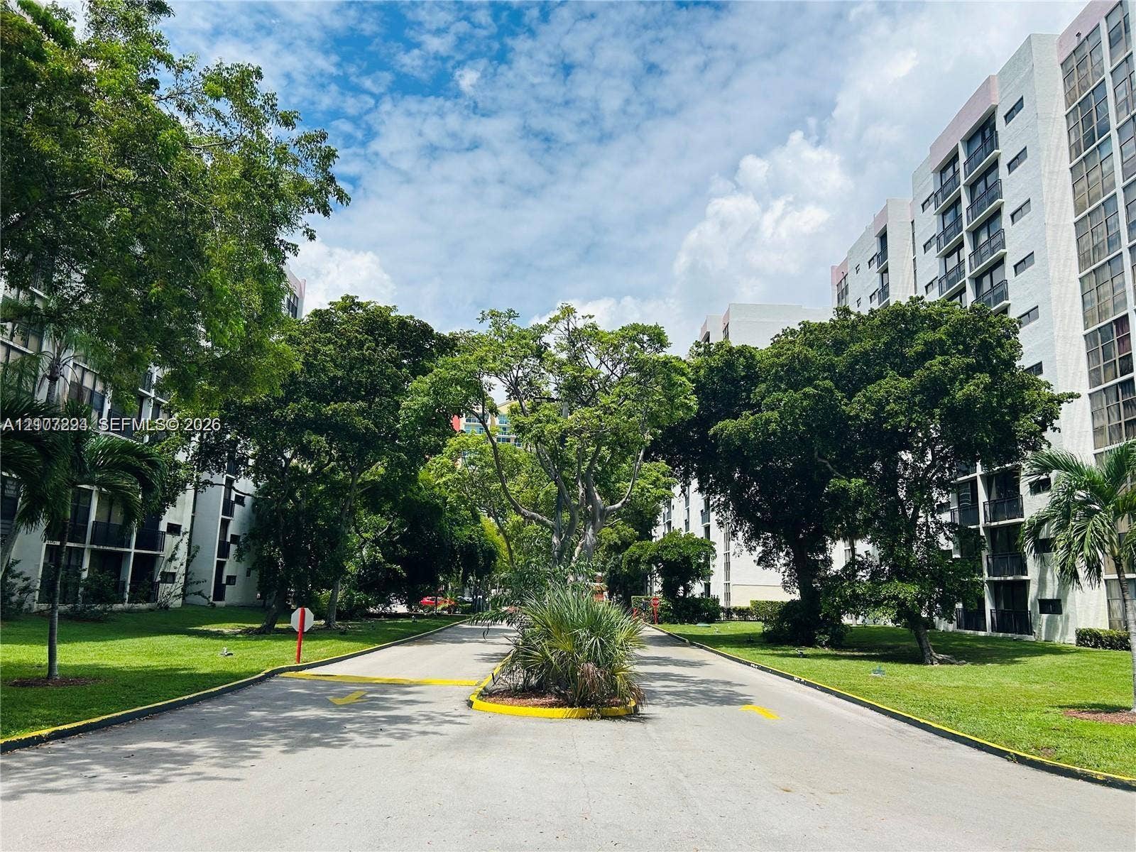 17021 N Bay Road, #219, Sunny Isles Beach, Sunny Isles Beach, FL 33160 Multi-story residential complex featuring white stucco facades, private balconies, expansive green space, mature canopy trees, and paved thoroughfares