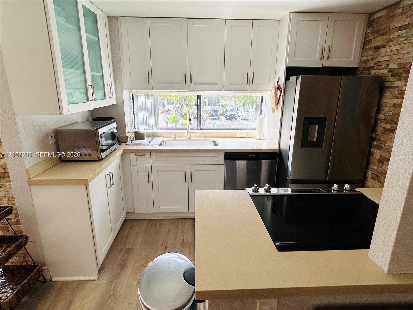 17021 N Bay Road, #219, Sunny Isles Beach, Sunny Isles Beach, FL 33160 Kitchen featuring white shaker-style cabinetry, solid-surface countertops, wood-finish flooring, a stainless steel refrigerator, and a stacked stone accent wall