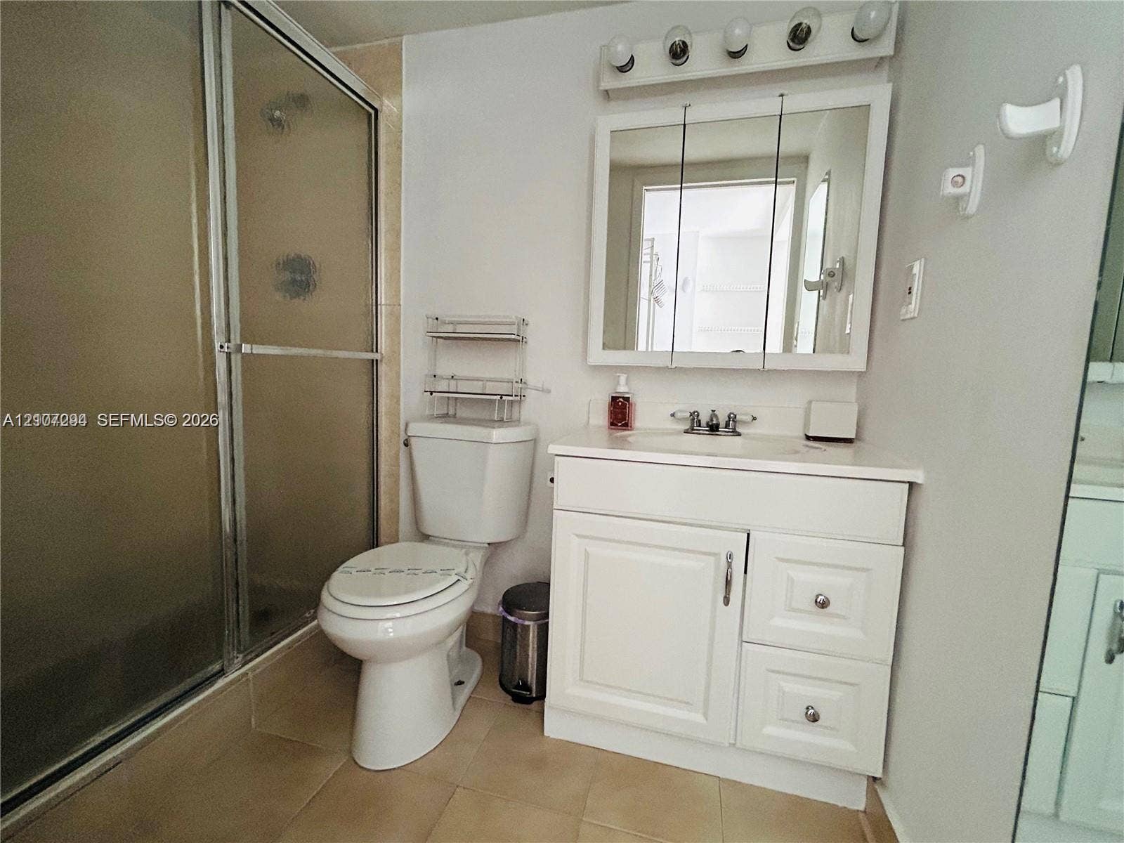 17021 N Bay Road, #219, Sunny Isles Beach, Sunny Isles Beach, FL 33160 Bathroom featuring a glass-enclosed shower, white vanity cabinet with stone-surfaced countertop, integrated sink, and triple-door medicine cabinet with integrated lighting