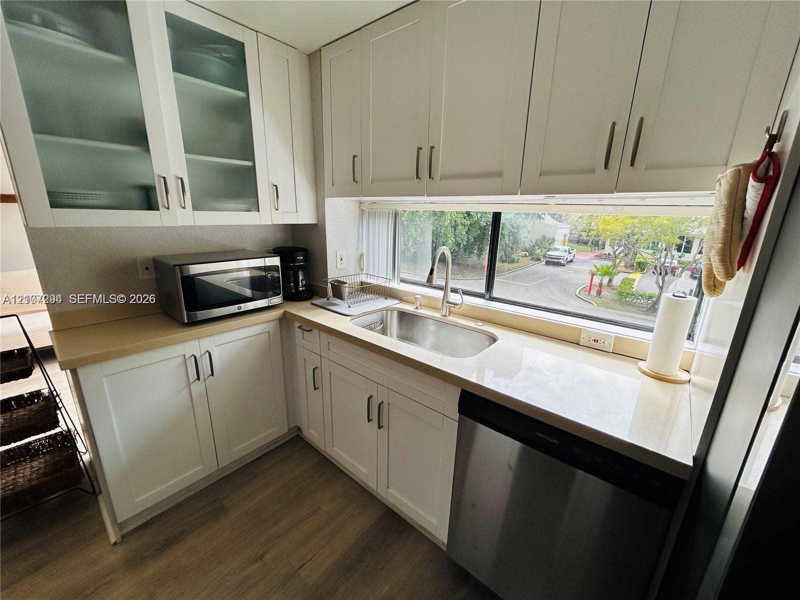 17021 N Bay Road, #219, Sunny Isles Beach, Sunny Isles Beach, FL 33160 Kitchen featuring shaker-style cabinetry with glass-front accents, solid-surface countertops, undermount stainless steel sink, stainless steel dishwasher, and wood-finish flooring