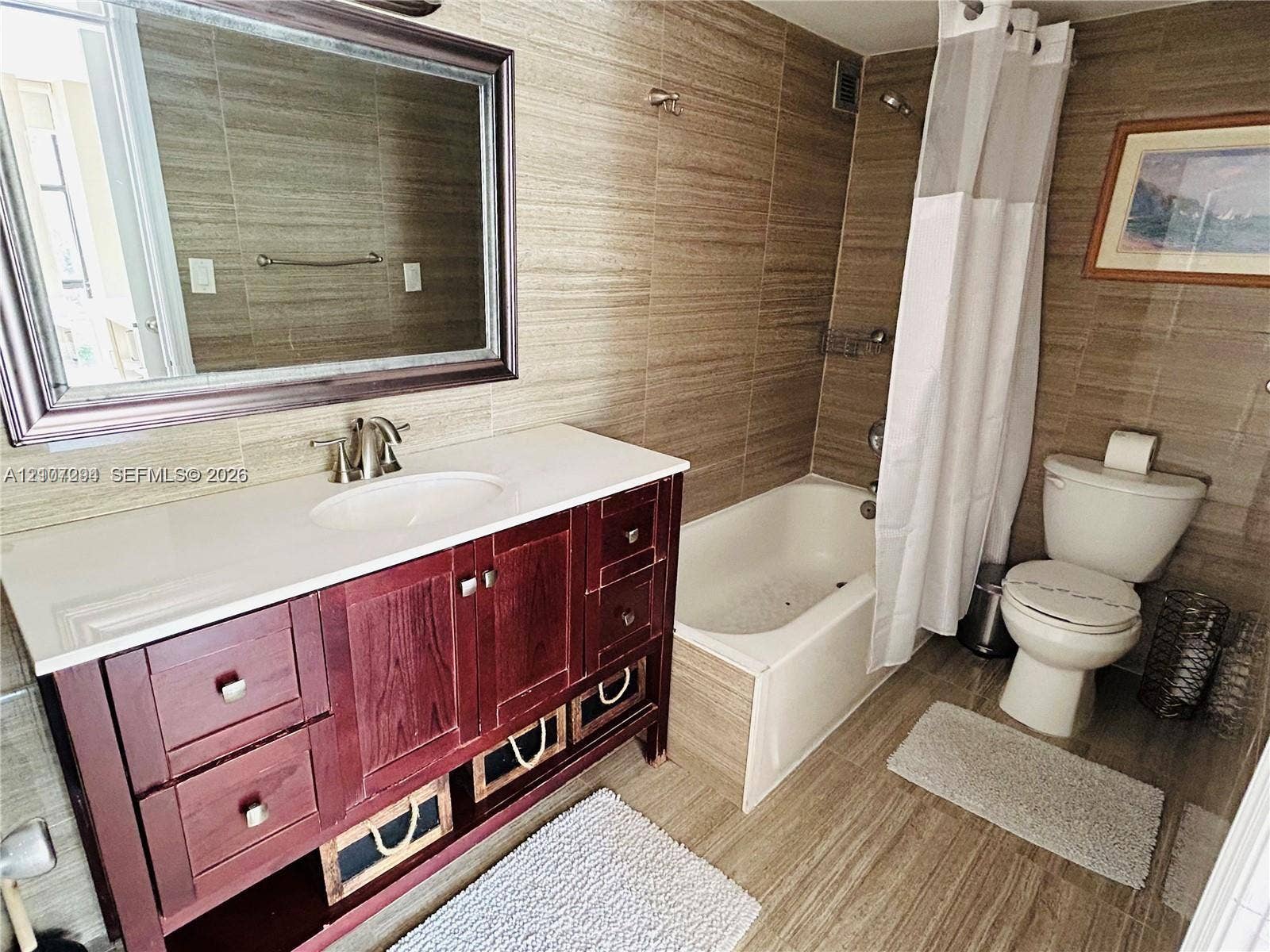 17021 N Bay Road, #219, Sunny Isles Beach, Sunny Isles Beach, FL 33160 Bathroom featuring a vanity with wood-finish cabinetry, white countertop with integrated sink, framed wall mirror, and floor-to-ceiling tile surrounding the tub and shower combination