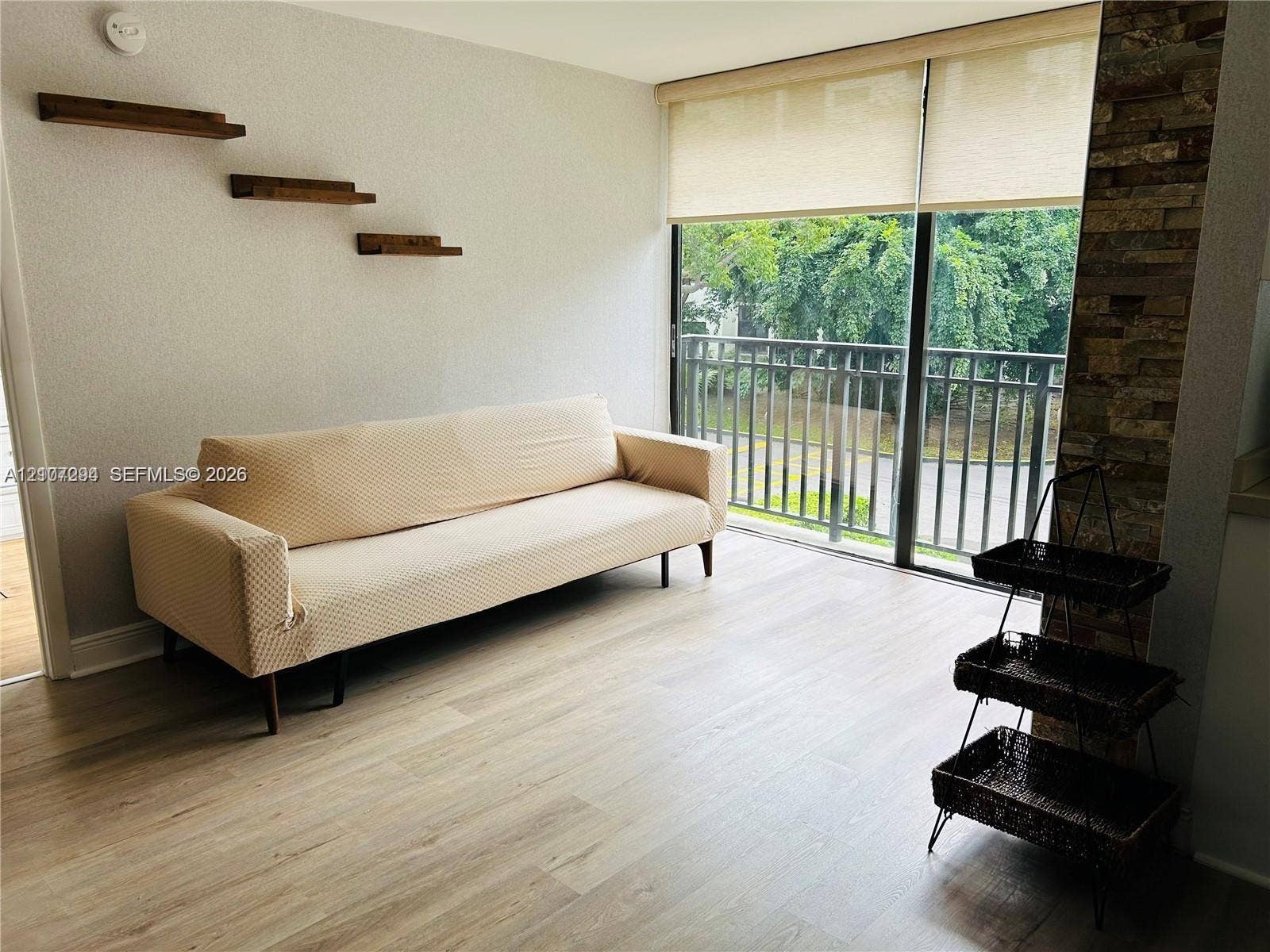 17021 N Bay Road, #219, Sunny Isles Beach, Sunny Isles Beach, FL 33160 Living area featuring wood-finish flooring, floor-to-ceiling sliding glass doors, built-in wooden wall shelves, and a floor-to-ceiling stacked stone accent pillar