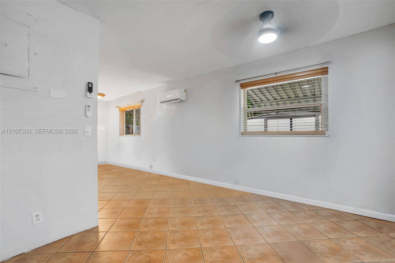 2051 NE 68th Street, Fort Lauderdale, FL 33308 Neutral-toned interior space featuring ceramic tile flooring, wall-mounted ductless air conditioning unit, ceiling-mounted lighting, and horizontal window blinds