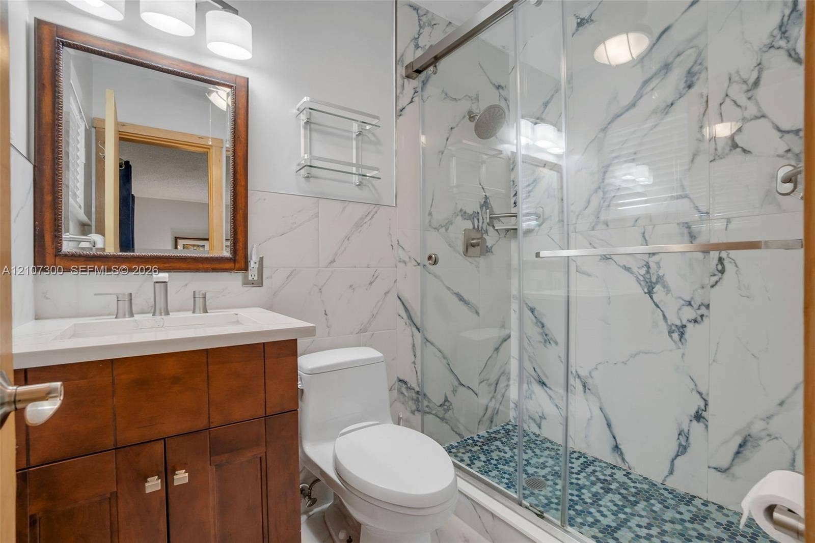 2051 NE 68th Street, Fort Lauderdale, FL 33308 Bathroom featuring a dark wood vanity with white countertop, rectangular undermount sink, shower with glass sliding door and large-format tile surround, and mosaic tile shower floor