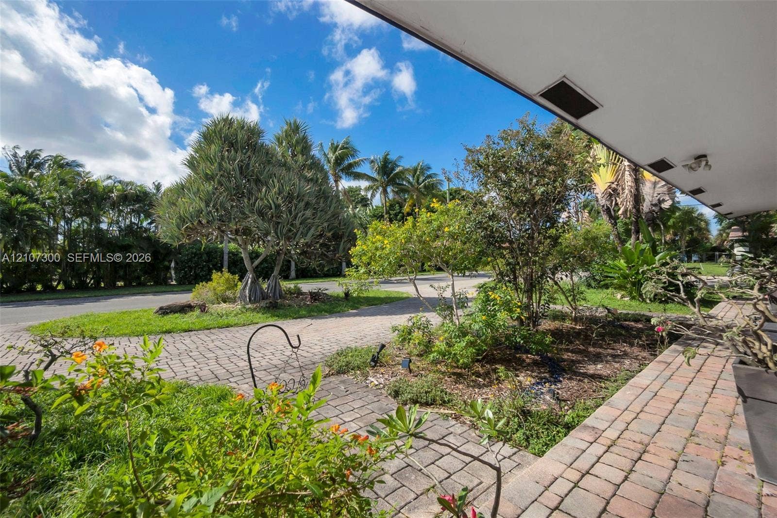 2051 NE 68th Street, Fort Lauderdale, FL 33308 Covered outdoor porch with stone-paver flooring, extensive mature landscaping, and multi-patterned stone-paver driveway