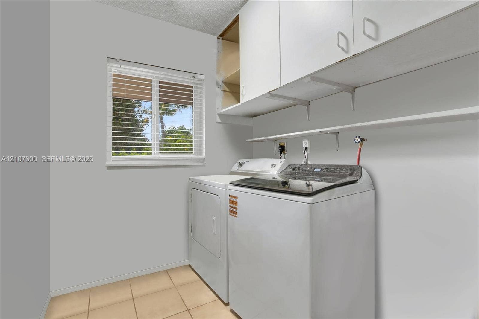2051 NE 68th Street, Fort Lauderdale, FL 33308 Utility area featuring overhead cabinetry, open shelving, tile flooring, and a single-pane window with horizontal blinds