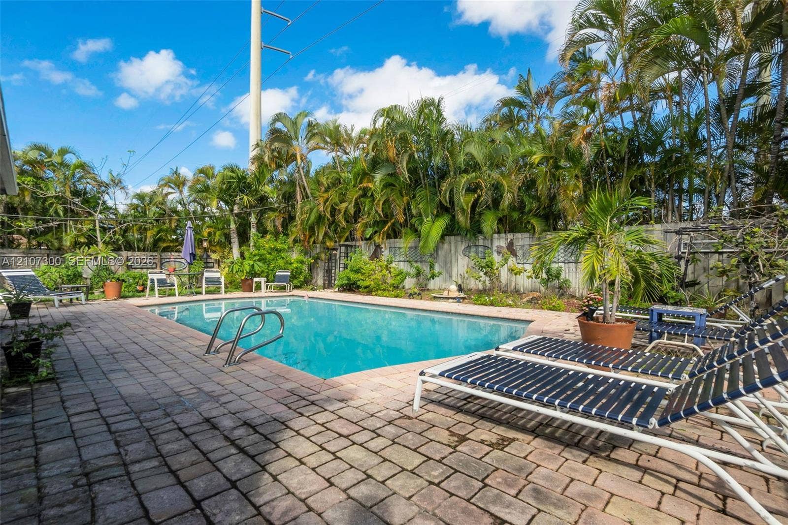 2051 NE 68th Street, Fort Lauderdale, FL 33308 In-ground swimming pool with metal ladder entry, surrounded by a brick-paver patio and privacy fencing