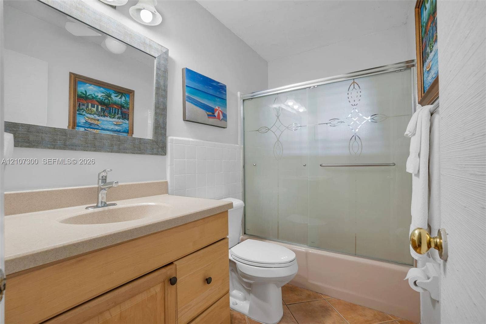 2051 NE 68th Street, Fort Lauderdale, FL 33308 Bathroom featuring a natural wood vanity with a solid-surface countertop, an integrated sink, a framed wall mirror, and a tub-shower combination with sliding frosted glass doors
