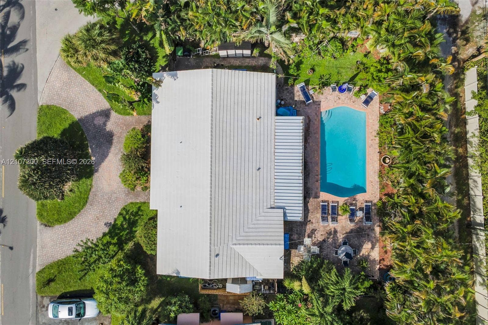 2051 NE 68th Street, Fort Lauderdale, FL 33308 Aerial view featuring a metal roof, paver driveway, swimming pool, paver patio, and mature perimeter landscaping