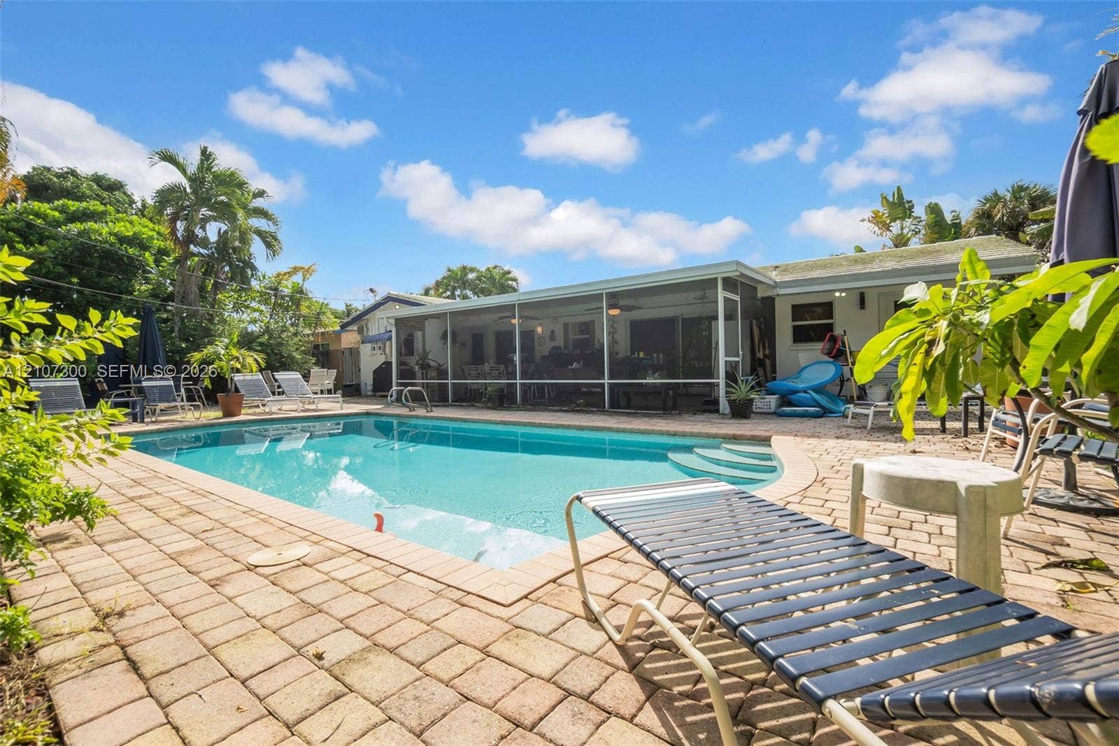 2051 NE 68th Street, Fort Lauderdale, FL 33308 In-ground pool featuring built-in stairs, enclosed screen lanai, and expansive paver patio