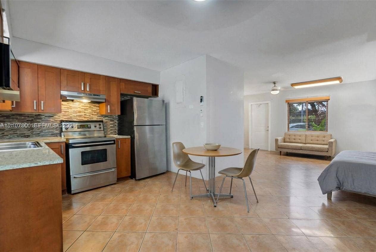 2051 NE 68th Street, Fort Lauderdale, FL 33308 Kitchen featuring flat-panel wood cabinetry, stone countertops, a mosaic tile backsplash, and stainless steel appliances, set against tile flooring