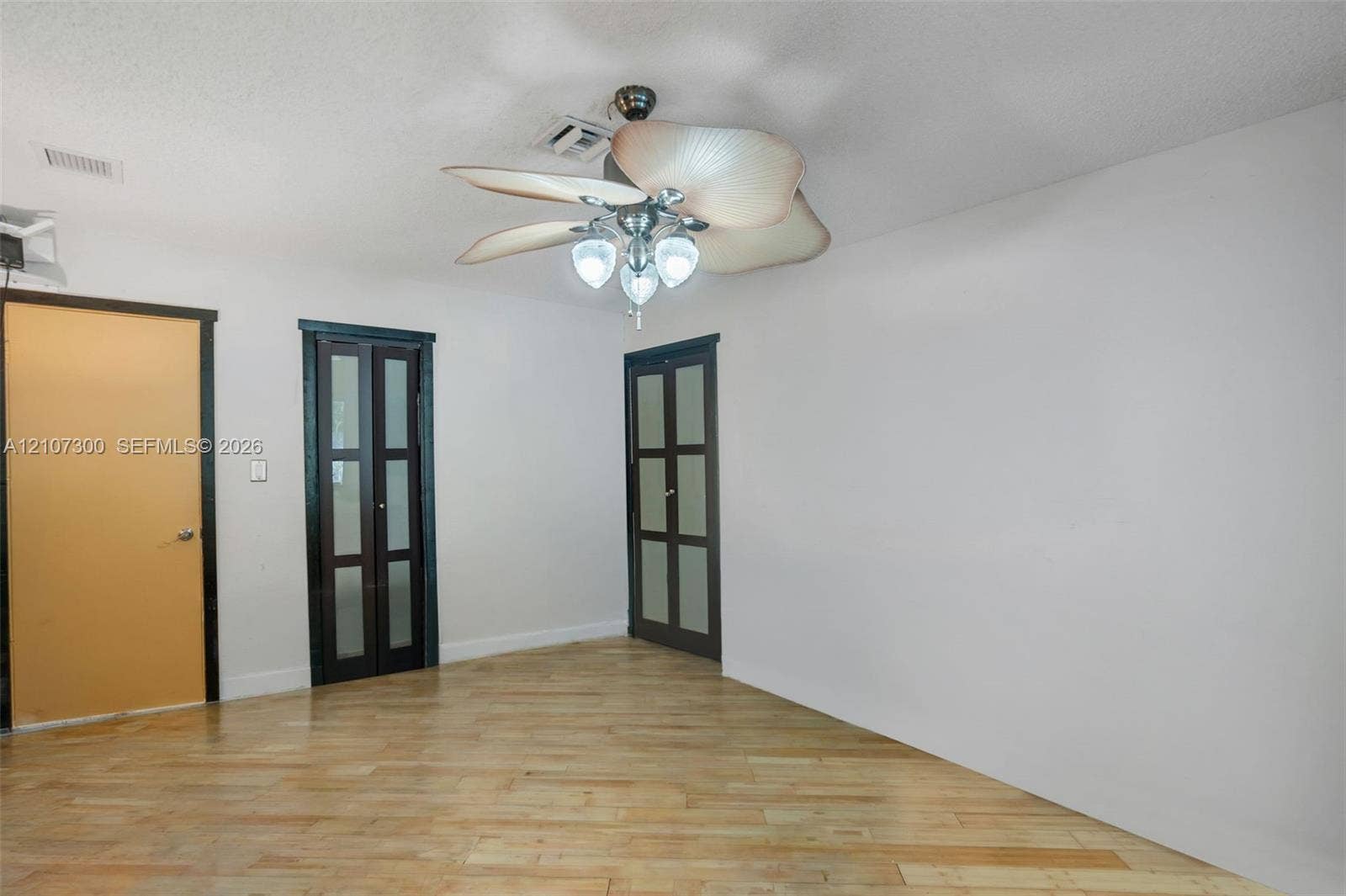 2051 NE 68th Street, Fort Lauderdale, FL 33308 Interior space featuring wood-finish flooring, a multi-blade ceiling fan with integrated lighting, and dual four-panel glass-inset doors with dark frames