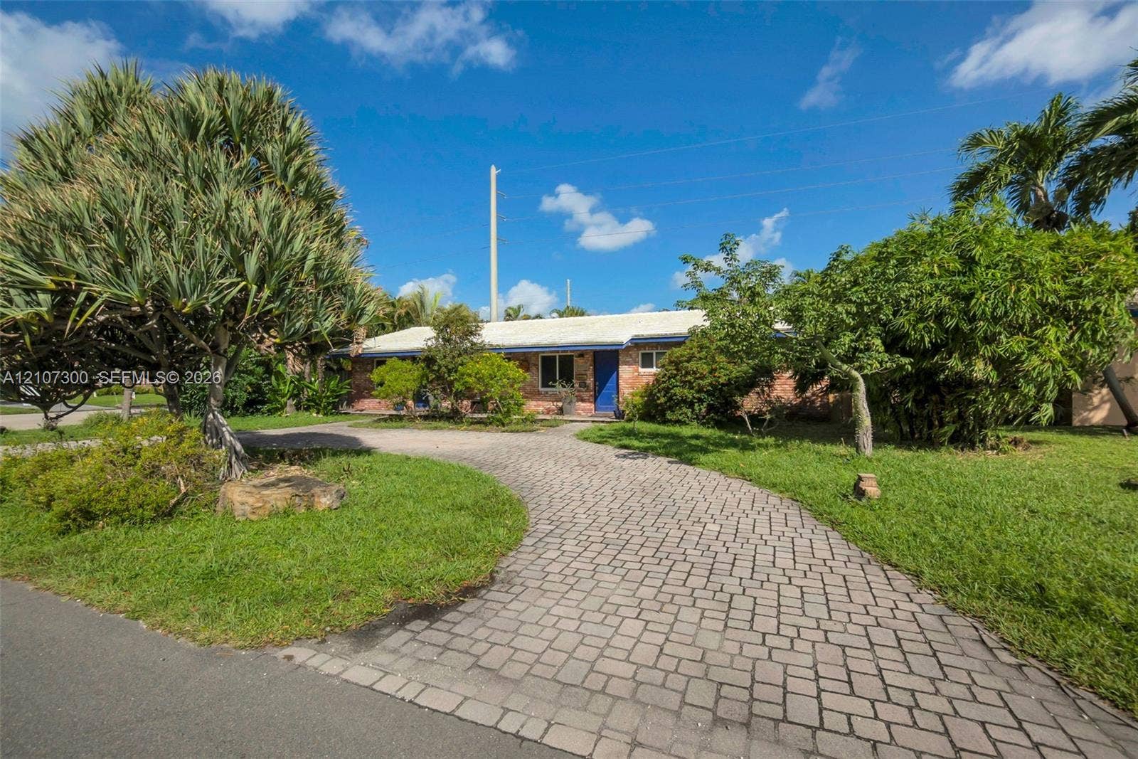 2051 NE 68th Street, Fort Lauderdale, FL 33308 Single-story brick exterior featuring a curved paver driveway, mature landscaping, and an expansive lawn