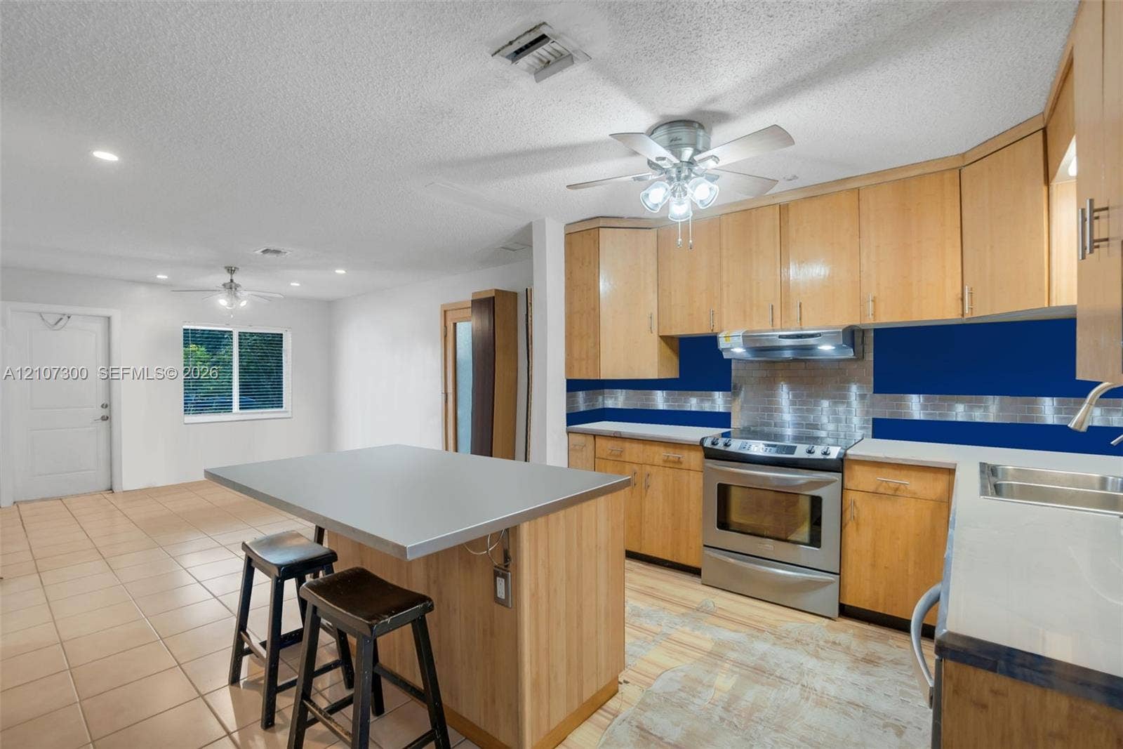 2051 NE 68th Street, Fort Lauderdale, FL 33308 Kitchen featuring wood cabinetry, a central island with a solid-surface countertop, stainless steel range with overhead vent hood, and tiled flooring