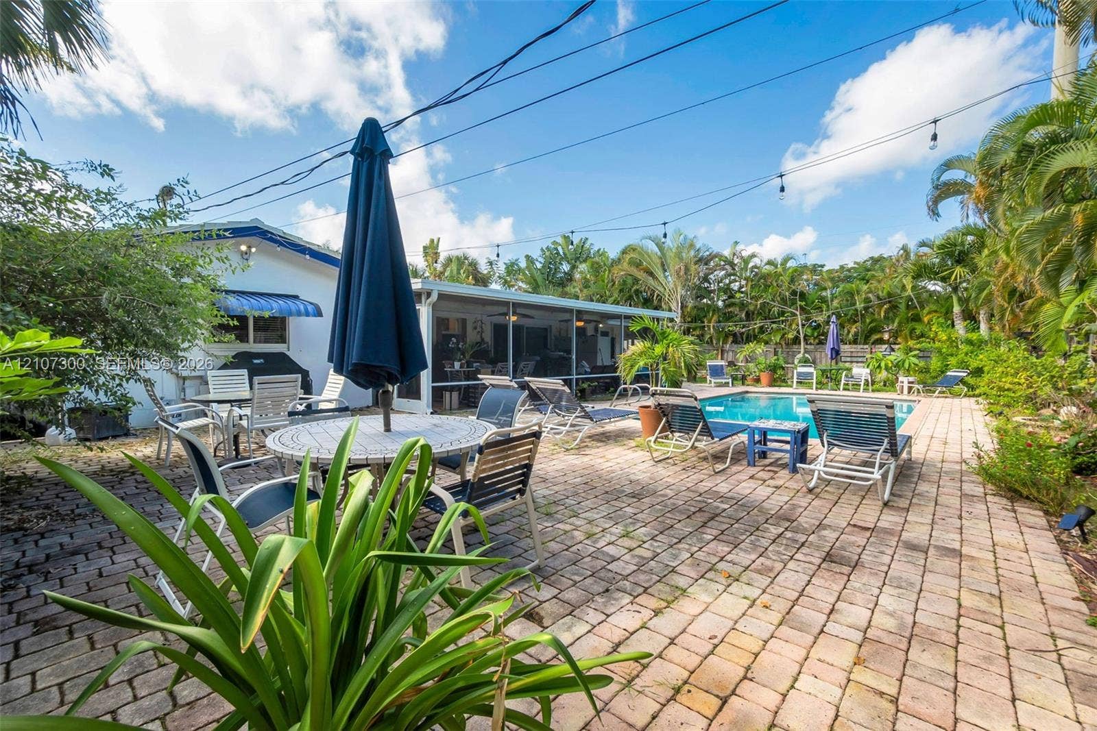 2051 NE 68th Street, Fort Lauderdale, FL 33308 Outdoor living space featuring a paver patio, screened-in lanai, and an in-ground swimming pool surrounded by mature palms